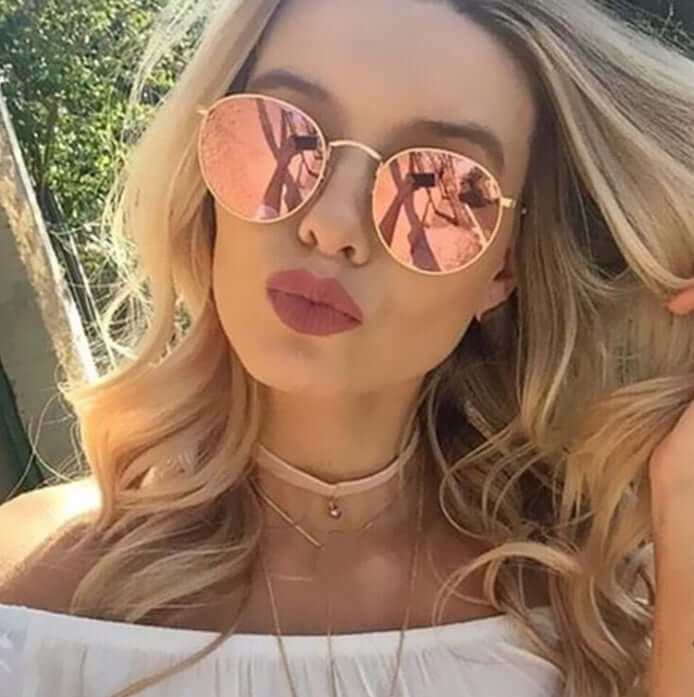 Woman wearing stylish sunglasses with round mirrored lenses, showcasing confidence and elegance.